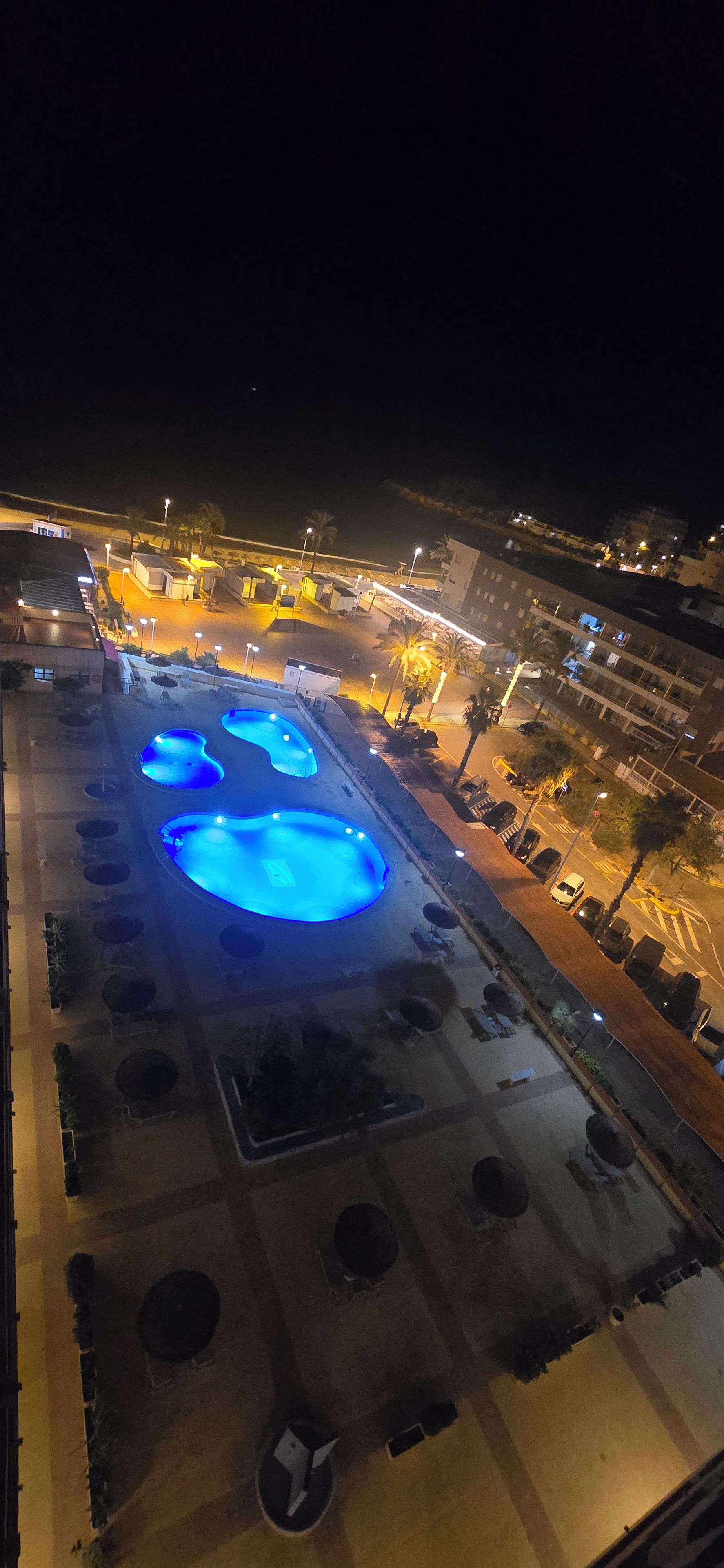 A nighttime view of a swimming pool complex with multiple pools and surrounding walkways.