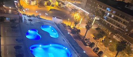 A nighttime view of a swimming pool complex with multiple pools and surrounding walkways.
