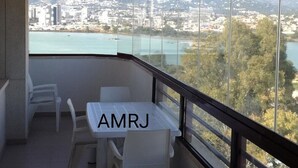 A balcony with a table and chairs, a view of a cityscape and mountains, and the text "AMRJ" on the table.