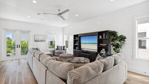 Un salon moderne avec un grand canapé d’angle, un téléviseur à écran plat et un ventilateur de plafond.