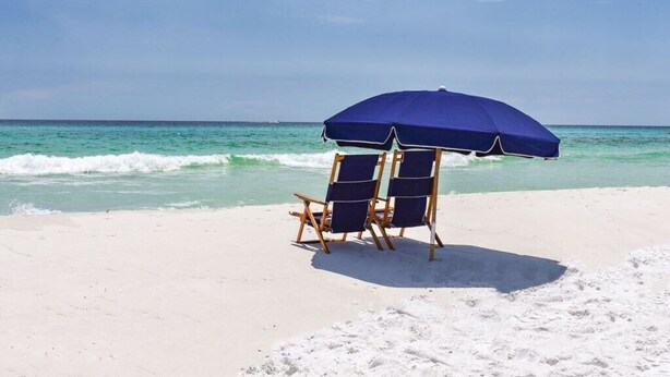 Une plage avec deux chaises de plage bleues sous un parasol bleu, donnant sur l’océan.