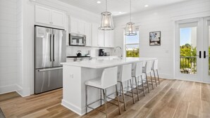 Une cuisine moderne avec des meubles blancs, des appareils en acier inoxydable et un grand îlot central doté de tabourets de bar.