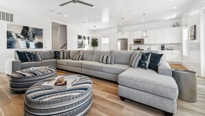 Un salon moderne avec un canapé d’angle gris, des poufs et un ventilateur de plafond.