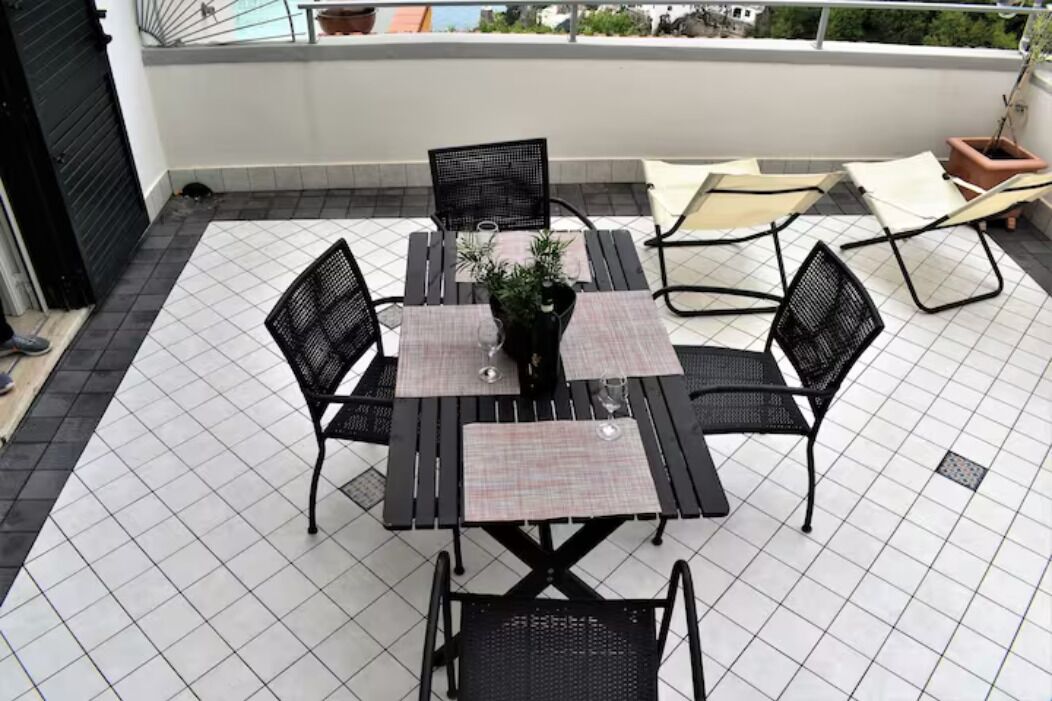 Une terrasse sur le toit, avec une table et des chaises en métal noir, un pot de fleurs et une vue sur le paysage urbain.