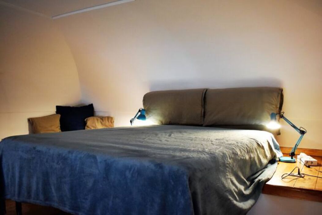 A bedroom with a bed, pillows, a desk, and a desk lamp.