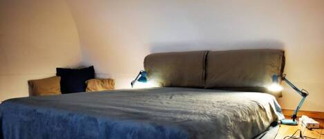 A bedroom with a bed, pillows, a desk, and a desk lamp.