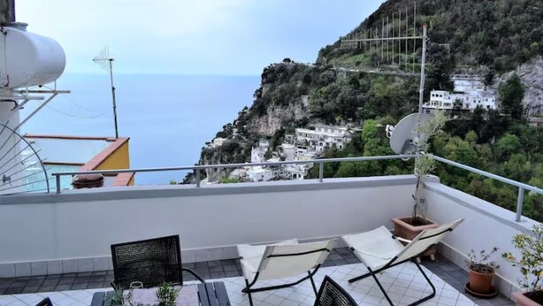 A balcony with outdoor furniture, a satellite dish, and a view of a coastal town with buildings on a hillside. - Chez Angelina Positano (Positano)
