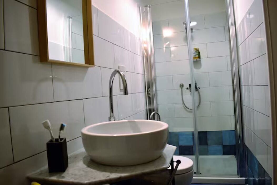 Un baño con un lavamanos grande blanco, un espejo y una zona de ducha.