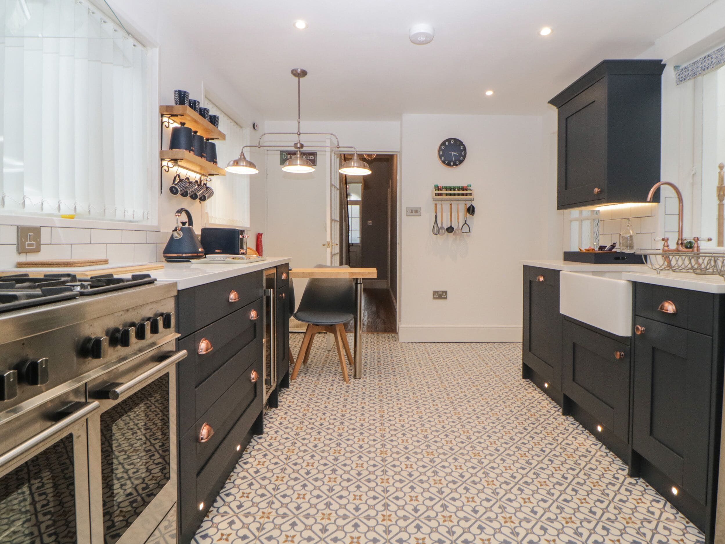 A modern kitchen with a stove, oven, and black cabinets. There is a dining area with a table and chairs, and a clock on the wall.