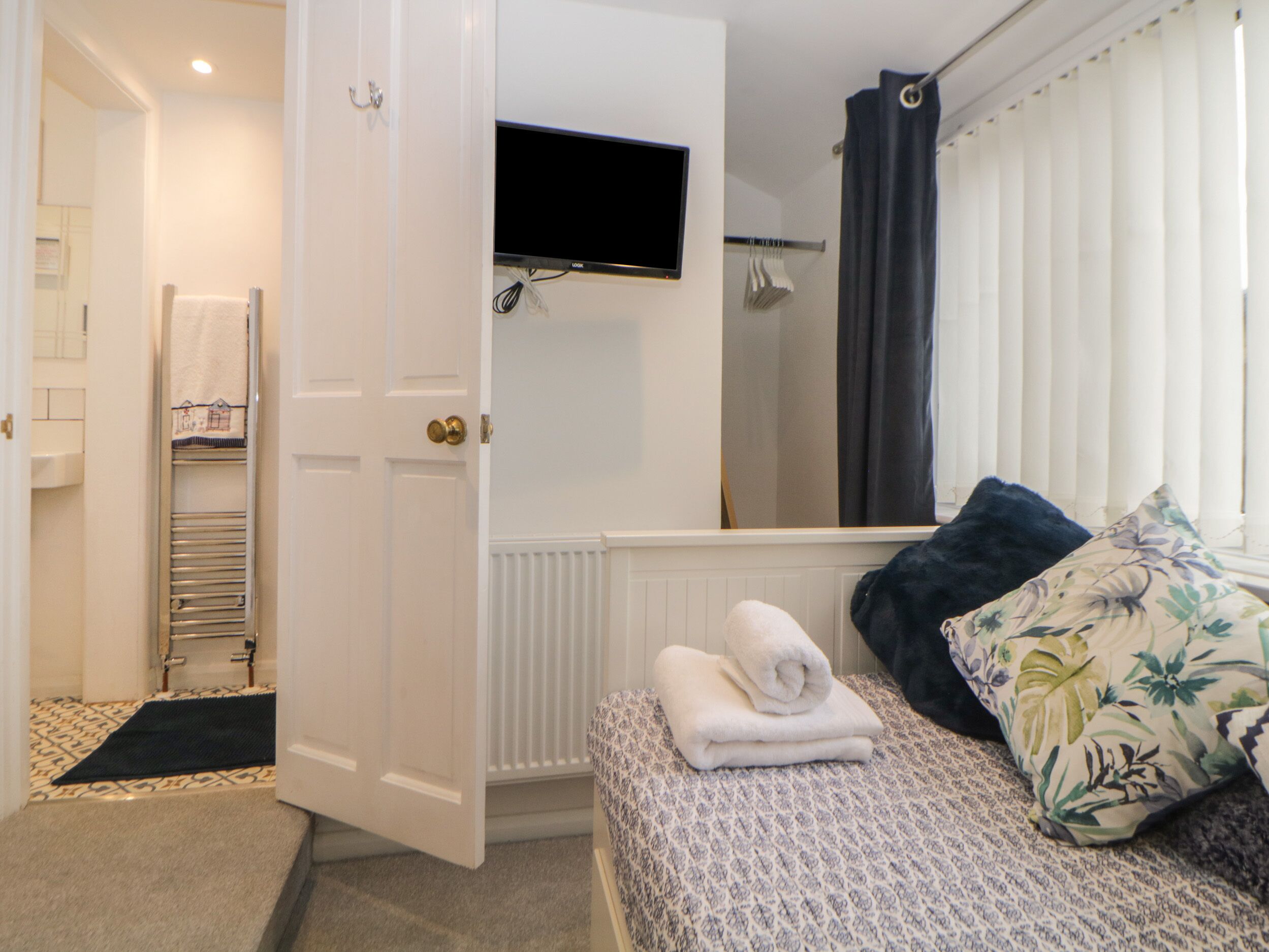 Une chambre d’hôtel avec un lit, un téléviseur fixé au-dessus, un porte-serviettes et un espace douche.