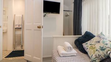 Une chambre d’hôtel avec un lit, un téléviseur fixé au-dessus, un porte-serviettes et un espace douche.