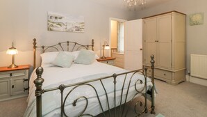 Un dormitorio con estructura de cama metálica, candelabro, mesita de noche con lámpara, armario y un cuadro en la pared.