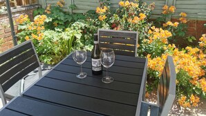 Una mesa exterior negra con dos copas de vino y una botella.