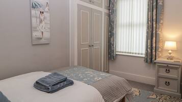 Un dormitorio con cama, una mesita de noche con lámpara, una ventana con cortinas y un cuadro en la pared.