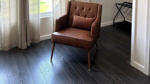 Une pièce avec un fauteuil en cuir marron, une fenêtre avec des rideaux beige et une armoire blanche dotée d’une tringle à vêtements.