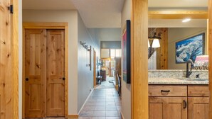 Un pasillo con puertas de madera, suelo de baldosas y una zona de cocina con encimeras de granito y armarios de madera.