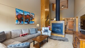 Un salón acogedor con sofá, sillón y mesa de centro. Hay una chimenea con repisa y un cuadro grande encima.