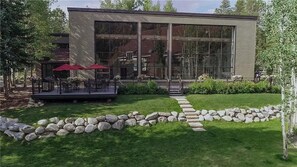 Un edificio moderno con amplios ventanales, un sendero de piedra y mobiliario exterior con sombrillas.