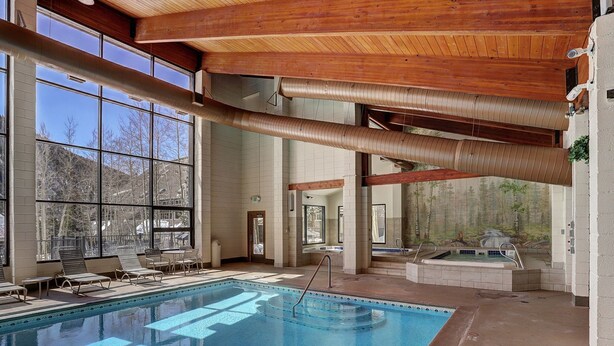 Una amplia piscina interior con agua cristalina, vigas de techo de madera y grandes ventanales que ofrecen vistas del paisaje circundante.