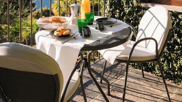 Um terraço com mesa posta para o pequeno-almoço, com vista para um lago e montanhas.