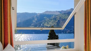 Quarto com uma grande janela que oferece vista para um lago e montanhas.