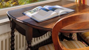 Quarto com vista para montanhas e um lago pela janela, uma mesa de madeira com um livro e uma cadeira com almofada listrada.