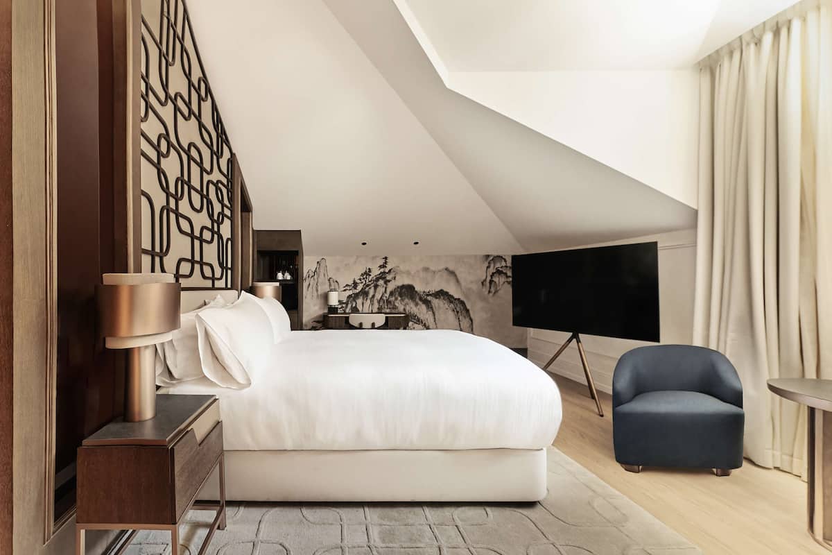 A modern bedroom with a large bed, a TV, a chair, and a decorative wall piece.