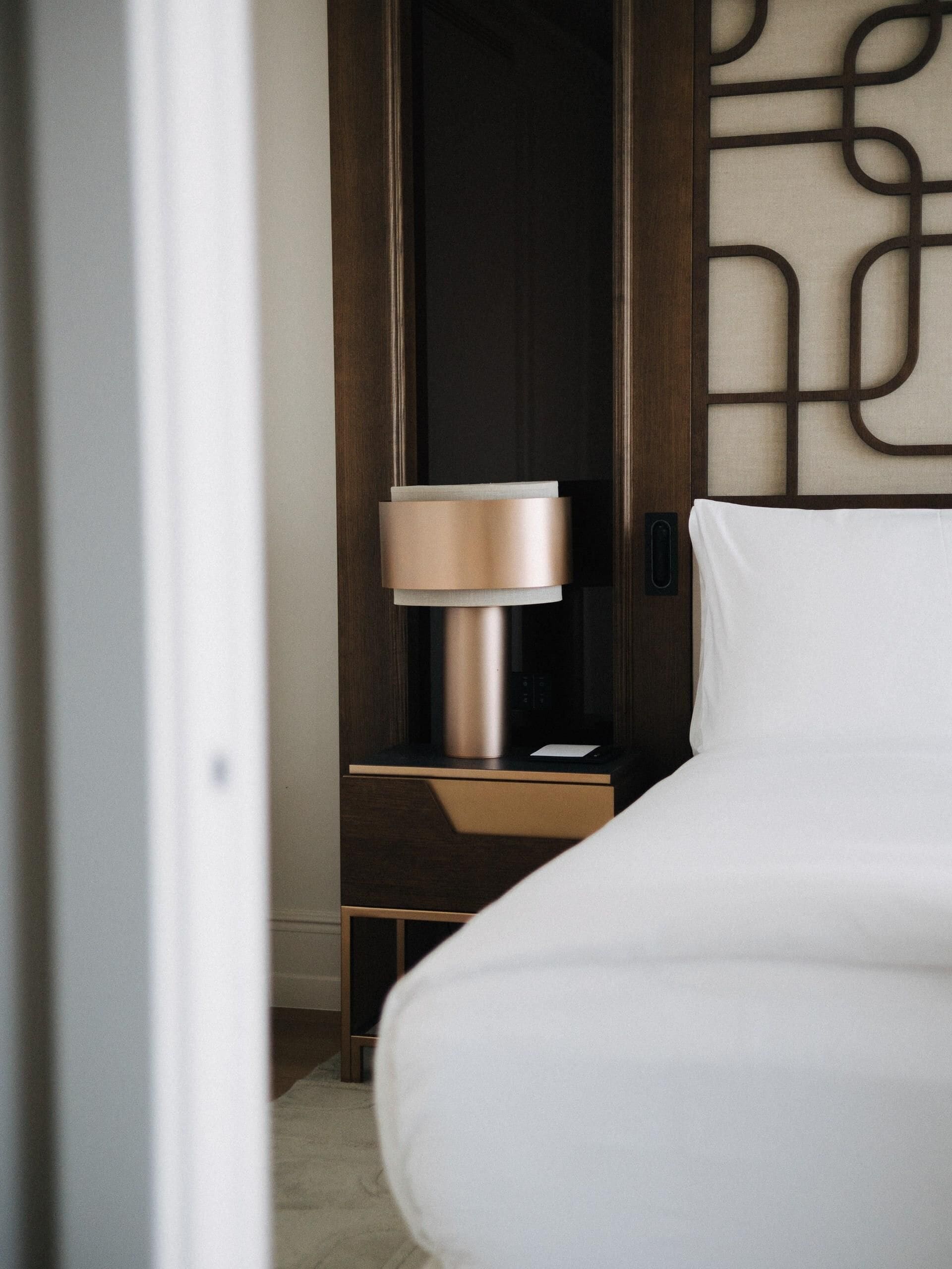 A modern hotel room with a bed, a nightstand, and a lamp.