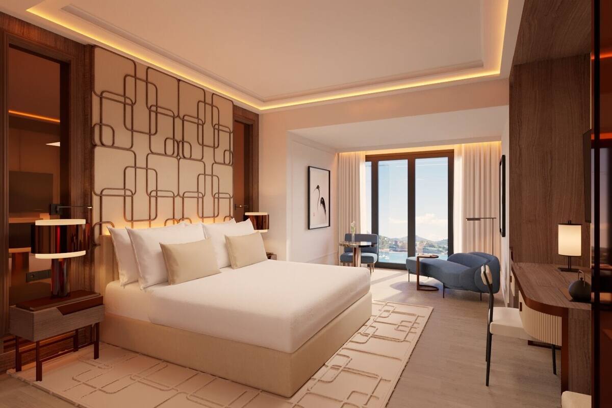 A modern hotel room with a large bed, a desk, and a view of the city.