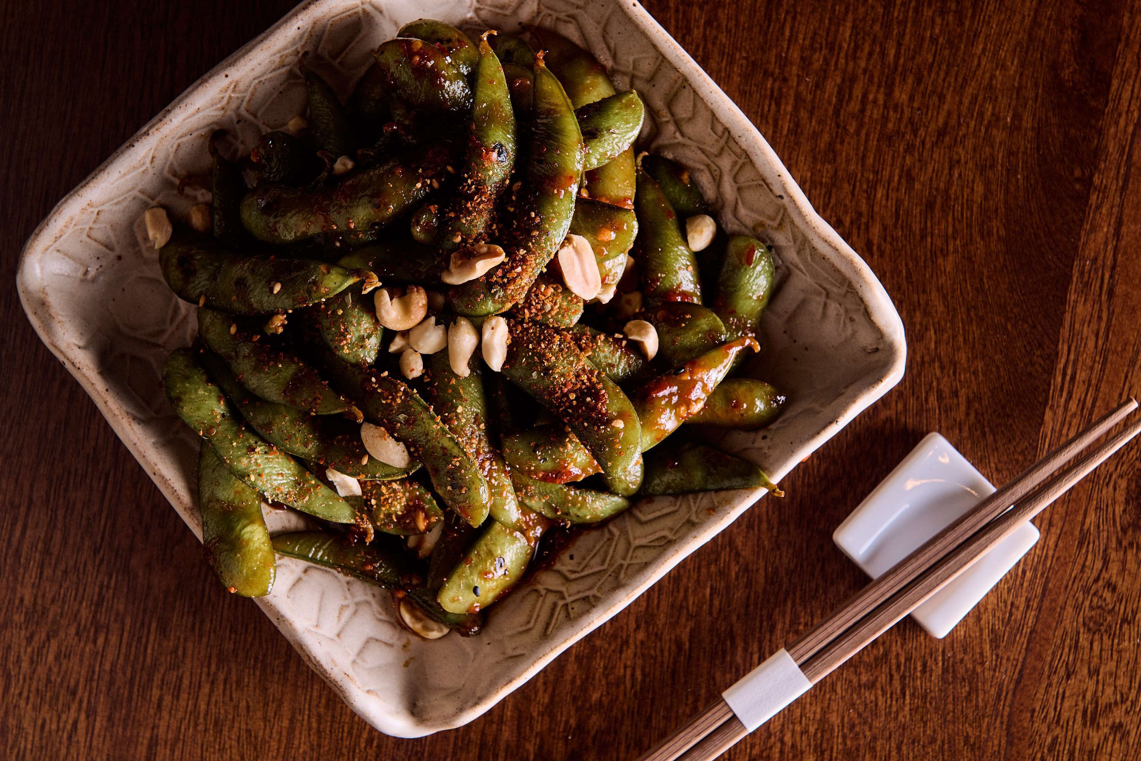 Un bol d'edamame condimentat amb cacauets damunt un tauler de fusta.