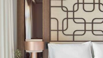 Habitación de hotel con cama, mesita de noche con lámpara, un panel decorativo en la pared y una puerta que da a otra habitación.