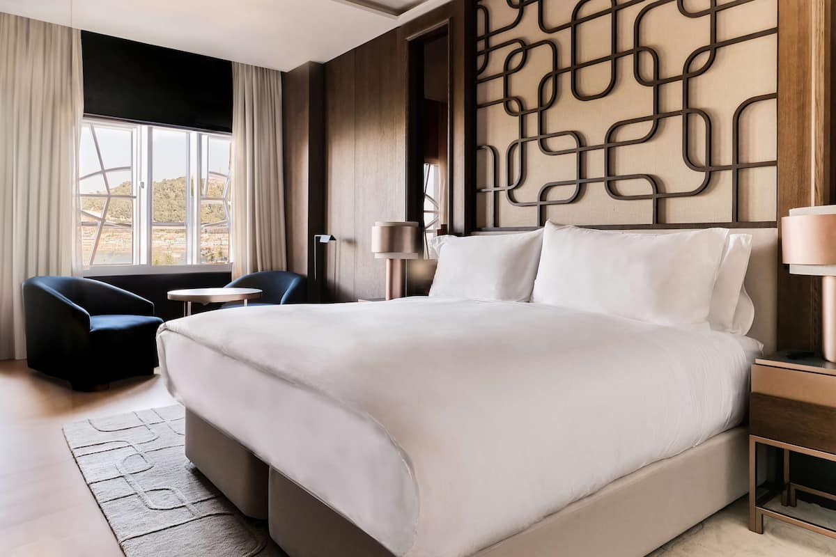 A hotel room with a large bed, a desk, a chair, and a view of a desert landscape.