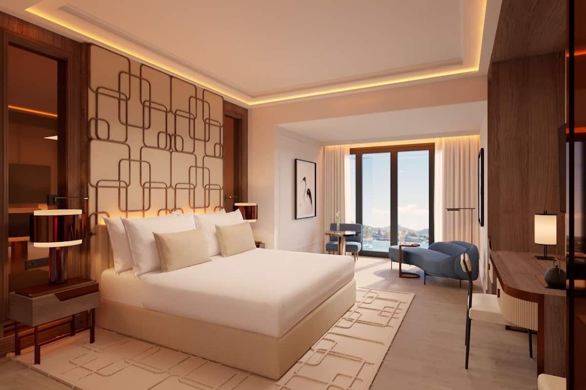 A modern hotel room with a large bed, a desk, and a view of the city.