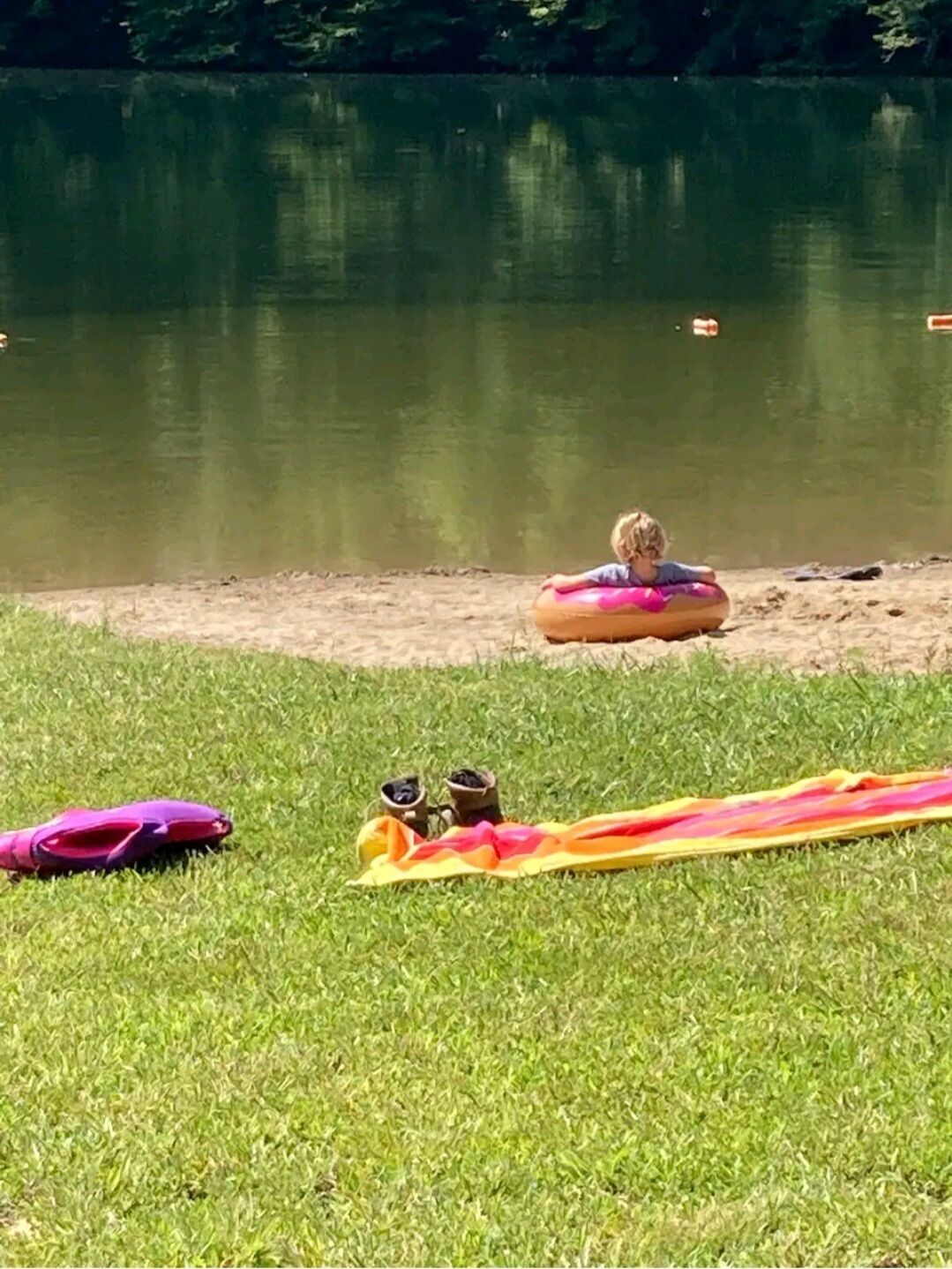 A grassy area with a water body, a child on a floating ring, and some items on the ground.