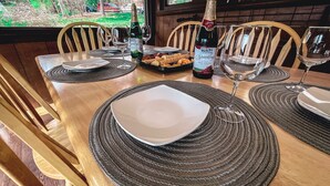 Une table de salle à manger en bois, mise avec des assiettes, des couverts et des verres, ainsi qu’une bouteille de vin rouge pétillant Welch’s et une boîte de collations.