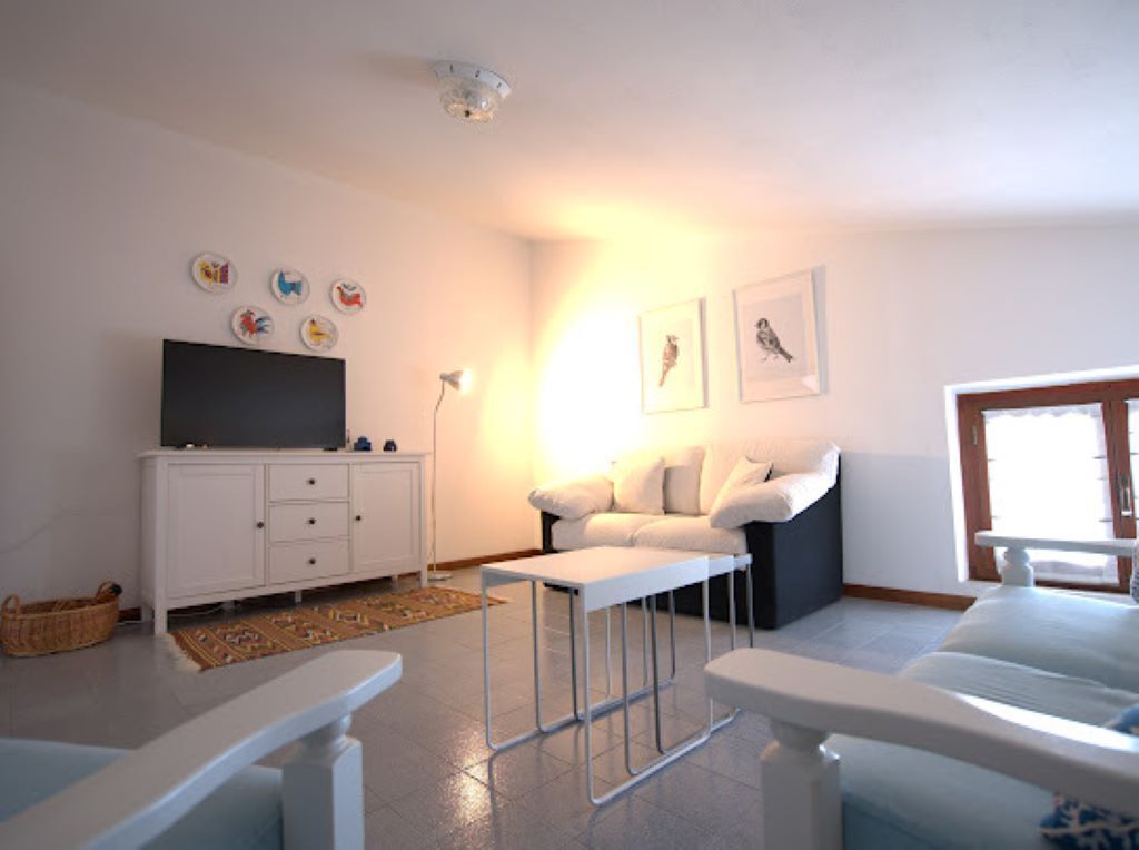 A modern living room with a flat-screen TV, white furniture, and artwork on the walls.