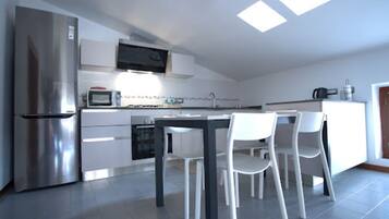 A modern kitchen with a stainless steel refrigerator, white cabinets, a microwave, and a dining area with white chairs.