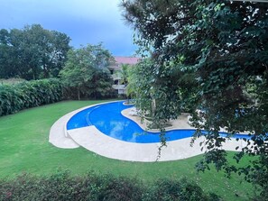 Una piscina de diseño curvo, rodeada de un césped cuidado y varios árboles.