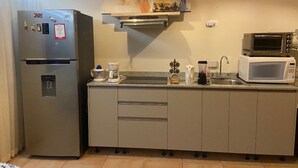 A kitchen with a refrigerator, microwave, coffee maker, and a painting on the wall. - CACAO SUITE IN CORONADO LUXURY  CLUB & SUITES - Kitchen & golf course A (Playa Coronado)