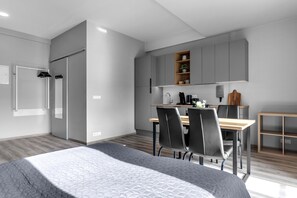 A modern bedroom with a large bed, a small desk, and a kitchenette.
