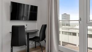 Ein modernes Zimmer mit einem wandmontierten Flachbildfernseher, einem Esstisch mit zwei Stühlen und einem großen Fenster mit Blick auf die Stadt und das Wasser.