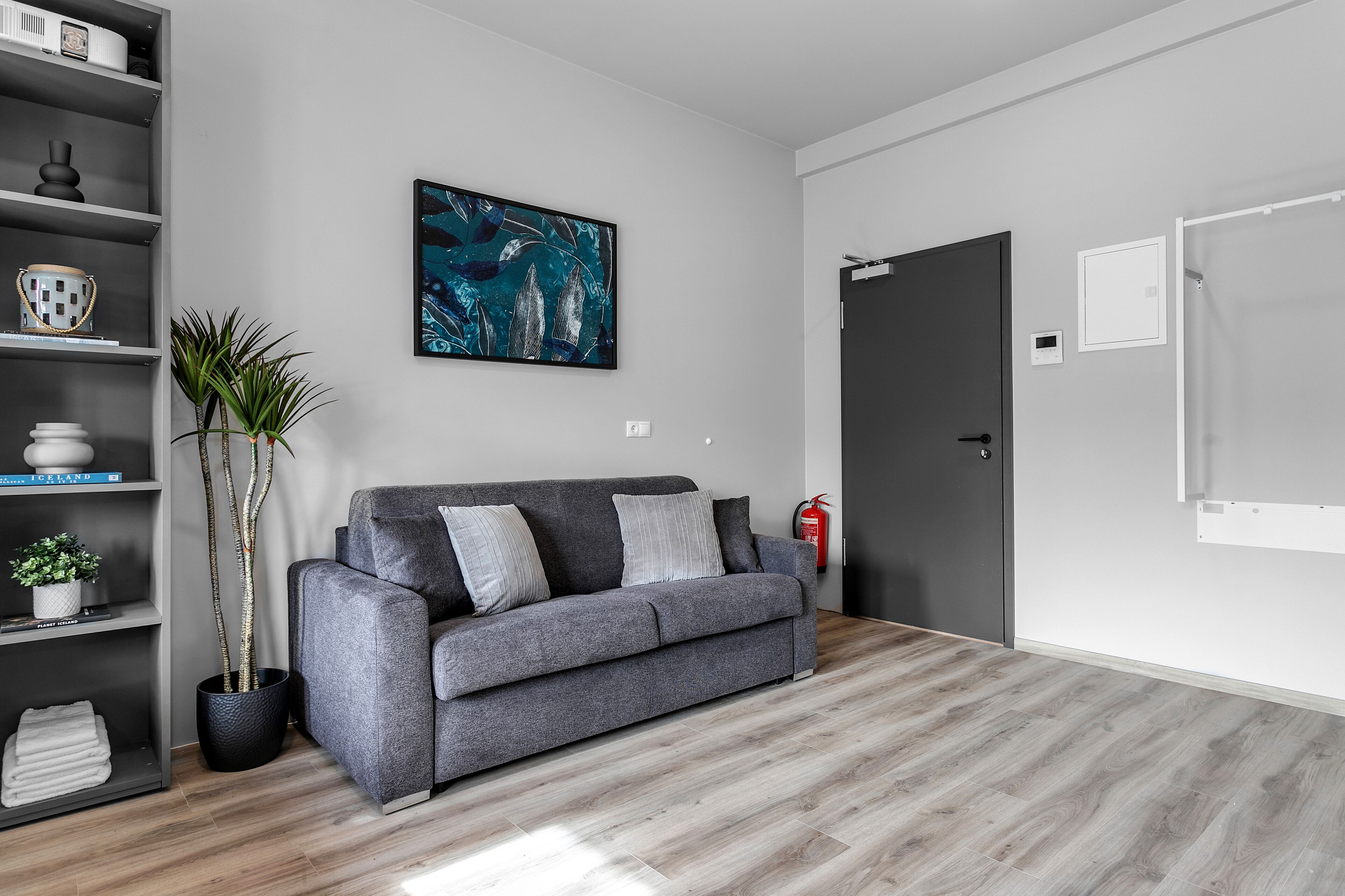 Una sala de estar moderna con un sofá gris, un cuadro abstracto grande, una planta en maceta y una estantería.