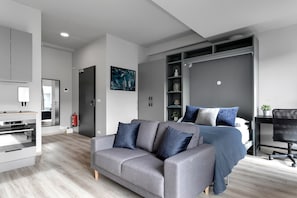 Un dormitorio moderno con un sofá gris, una cama con ropa de cama azul, un armario empotrado y un escritorio con una silla.