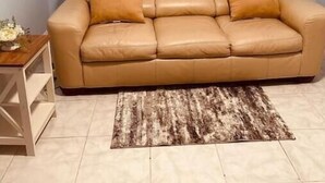 A beige leather sofa with two cushions, a wooden side table with a vase, and a patterned rug on a tiled floor. - Sunny and cozy place (Delray Beach)