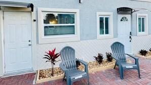 A building with a white door, a window with blinds, and a small garden area with plants and two chairs. - Sunny and cozy place (Delray Beach)