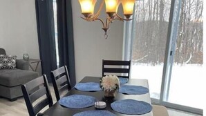 Un coin repas avec une table dressée pour six personnes, entourée de chaises en bois foncé dotées d’assises rembourrées. Un lustre à trois lampes est suspendu au-dessus de la table.