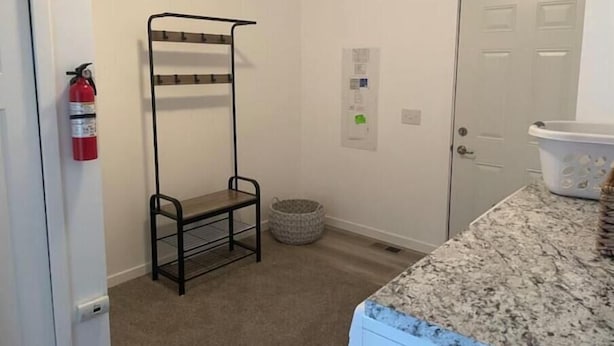 Een kleine, schone kamer met een metalen rek, een brandblusser, een deur en een wasmand.