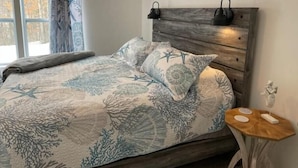 Une chambre à coucher avec un lit, une table de chevet, une lampe fixée au mur et une fenêtre avec des rideaux.