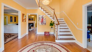 A spacious foyer with a wooden staircase, a chandelier, and a large rug.