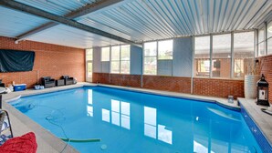 An indoor swimming pool with a brick wall, large windows, and a metal roof.